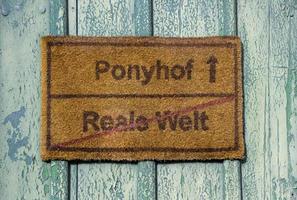 señal de tráfico en alemán que dice ponyhof y reale welt jugando con el equivalente alemán al dicho la vida no es un picnic escolar dominical. foto