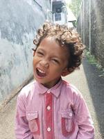 Photo of an expressive boy with curly curls in a red shirt