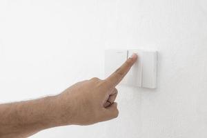 Close-up light switch of a male finger will turn on or off a light switch with white wall at home. white plastic mechanical switch mounted. Energy, energy, save electricity, copy space photo