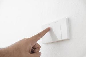 Close-up light switch of a male finger will turn on or off a light switch with white wall at home. white plastic mechanical switch mounted. Energy, energy, save electricity, copy space photo