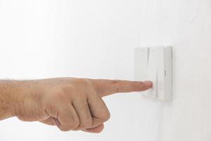 el interruptor de luz de primer plano de un dedo masculino encenderá o apagará un interruptor de luz con una pared blanca en casa. Interruptor mecánico de plástico blanco montado. energía, energía, ahorrar electricidad, copiar espacio foto