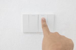 Close-up light switch of a male finger will turn on or off a light switch with white wall at home. white plastic mechanical switch mounted. Energy, energy, save electricity, copy space photo