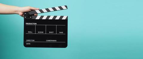 Hand is holding Black clapper board or movie slate on pastel blue or Tiffany Blue background. photo