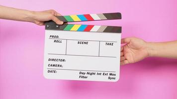 Hand is holding clapper board and sending clapperboard to other hand on pink background. photo