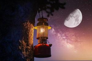 lámpara de aceite vintage colgada de un árbol en el bosque en el ambiente de campamento nocturno, concepto de viaje al aire libre imagen luna y estrellas fondo de galaxia foto