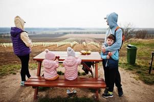 Family with children sit at wooden table against vineyard. photo