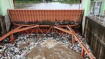 antenne visie van troebel bruin Woud water vrijgelaten door beton dam afvoer kanalen net zo water overstroomt in de regenachtig seizoen met droog twijgen en plastic verspilling Bij een dam poort in landelijk noordelijk Thailand. video