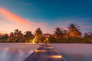 Sunset on Maldives island, luxury water villas resort, closeup wooden pier. Amazing colorful sky clouds, seaside beach, summer vacation holiday and exotic travel concept. Paradise sunset landscape photo