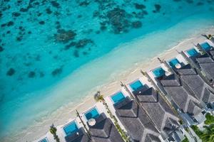 Aerial top view of pool villas, bungalows in Maldives paradise tropical beach. Amazing blue turquoise sea lagoon, ocean bay water. Luxury travel vacation destination. Beautiful sunny aerial landscape photo