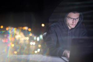 hacker using laptop computer while working in dark office photo