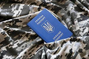 SUMY, UKRAINE - MARCH 20, 2022 Ukrainian foreign passport on fabric with texture of military pixeled camouflage. Cloth with camo pattern in grey, brown and green pixel shapes and Ukrainian ID photo