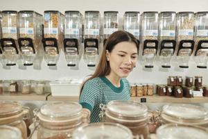 una joven cliente caucásica elige y compra productos orgánicos en frascos de vidrio reutilizables en la tienda de recarga, supermercado sin desperdicio y estilos de vida sostenibles, ecológicos y sin plástico. foto