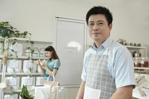 Portrait of an Asian male shopkeeper smiling and looking at camera, arranges natural products at refill store, zero-waste grocery, and plastic-free, eco environment-friendly, sustainable lifestyles. photo