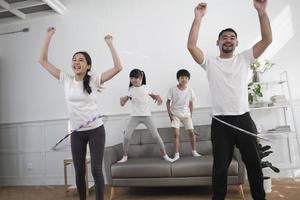 Happy wellness Asian Thai family, parents, and children are fun playing hula hoops together, fitness training and healthy exercise in white living room, domestic home lifestyle, and weekend activity. photo