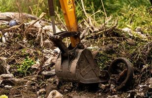 Backhoe digging soil at construction site. Bucket of backhoe digging soil. Clearing and grubbing. Digger working at road construction site. Earth moving machine. Excavation vehicle. Land development. photo