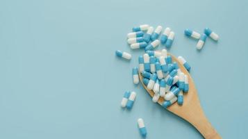 Blue-white antibiotic capsule pills on wooden spoon and blue background. Antibiotic drug resistance. Prescription drug. Medical care. Pharmaceutical care. Antimicrobial drug. World Pharmacist Day. photo