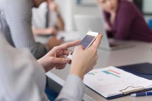 Cerca de las manos de una mujer de negocios usando un teléfono inteligente en una reunión foto