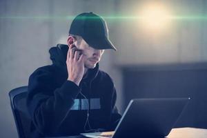 young talented hacker using laptop computer while working in dark office photo