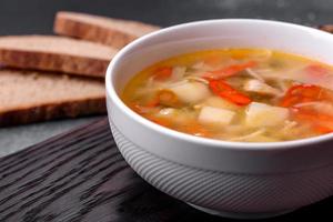 Closeup of a bowl of chicken noodle and vegetable soup on a concrete table photo