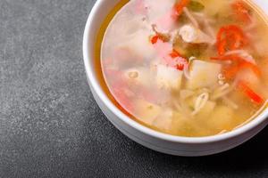 Closeup of a bowl of chicken noodle and vegetable soup on a concrete table photo