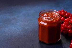 Viburnum fruit jam in a glass jar on a dark concrete background photo