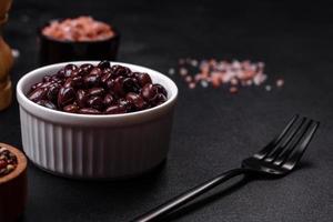 Black, canned beans in a white saucer against a dark concrete background photo