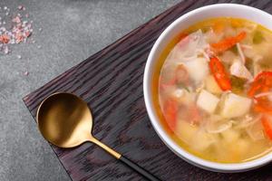 Closeup of a bowl of chicken noodle and vegetable soup on a concrete table photo