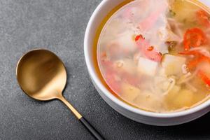 Closeup of a bowl of chicken noodle and vegetable soup on a concrete table photo