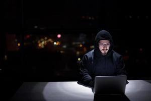 hacker using laptop computer while working in dark office photo