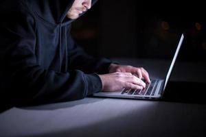 hacker using laptop computer while working in dark office photo