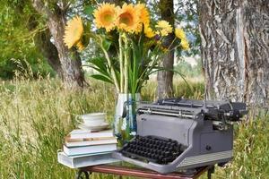 Vintage Typewriter With Vase Of Sunflowers, A Stack Of Books, And A Tea Cup photo