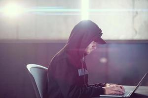 young talented hacker using laptop computer while working in dark office photo