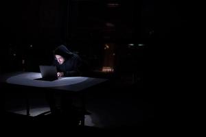 hacker using laptop computer while working in dark office photo