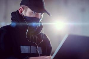 young talented hacker using laptop computer while working in dark office photo