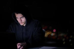 hacker using laptop computer while working in dark office photo