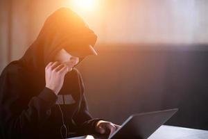 young talented hacker using laptop computer while working in dark office photo