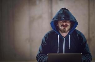 young hacker using laptop computer while working in dark office photo