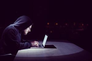 hacker using laptop computer while working in dark office photo