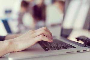 close up of business womans hand typing on laptop with team on meeting in background photo