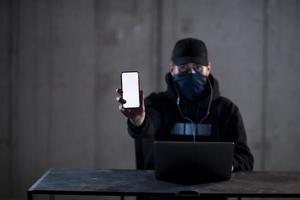 criminal hacker using laptop computer while working in dark office photo