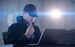 young talented hacker using laptop computer while working in dark office photo