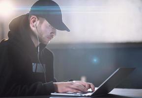 young talented hacker using laptop computer while working in dark office photo