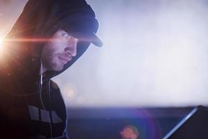 young talented hacker using laptop computer while working in dark office photo