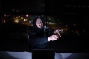 hacker using laptop computer while working in dark office photo