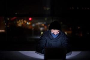 hacker using laptop computer while working in dark office photo