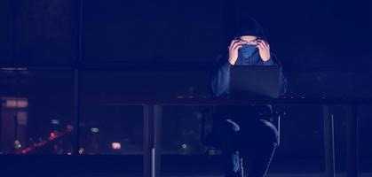 hacker using laptop computer while working in dark office photo