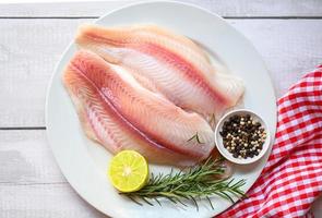 fresh raw pangasius fish fillet with herb and spices lemon lime and rosemary, meat dolly fish tilapia striped catfish, fish fillet on white plate with ingredients for cooking - top view photo