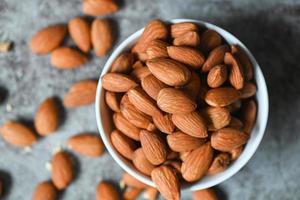 Almonds nuts top view - on white bowl, Delicious sweet almonds on the table dark background, roasted almond nut for healthy food and snack photo