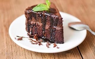 pastel de salsa de chocolate delicioso postre servido en la mesa - rebanada de pastel en un plato blanco con cobertura de chocolate y hoja de menta foto