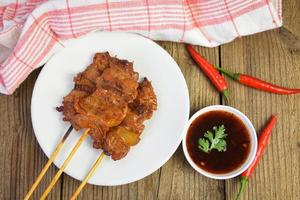 Brocheta de cerdo a la parrilla con salsa en la placa blanca de cerdo satay menú de comida tailandesa e indonesia asiática foto